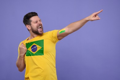 Image of Excited fan with flag of Brazil on his t-shirt against dark violet background. Space for text