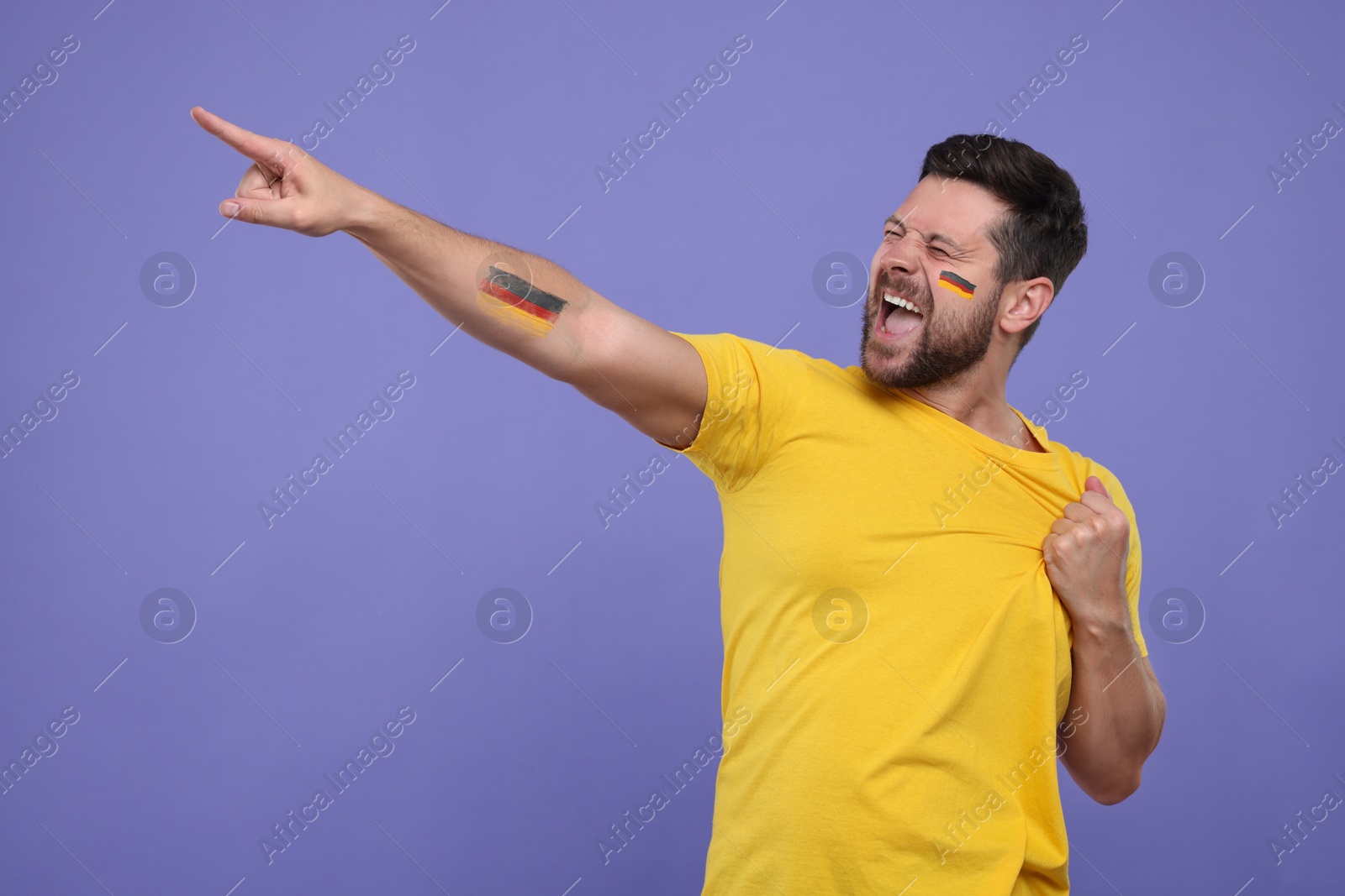 Excited fan with flags of Germany painted on his cheek and arm against dark violet background. Space for text Image of Excited fan with flags of Germany painted on his cheek and arm against dark violet background. Space for text