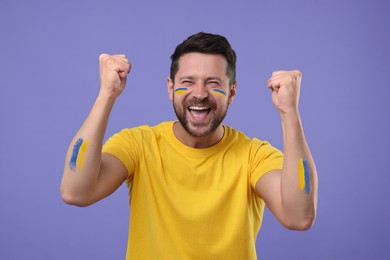 Image of Happy fan with flags of Ukraine painted on his body against dark violet background
