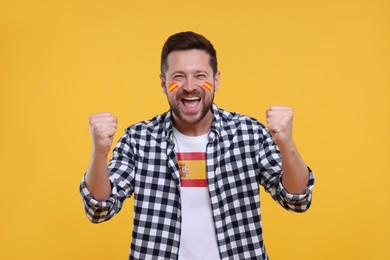 Image of Happy fan with flag of Spain on his t-shirt against orange background