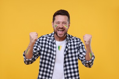Image of Happy fan with flag of Brazil painted on his face against orange background