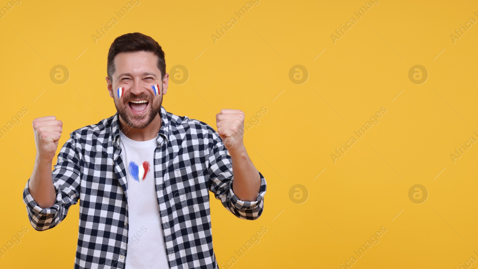 Happy fan with flags of France on his face and t-shirt against orange background. Banner design with space for text Image of Happy fan with flags of France on his face and t-shirt against orange background. Banner design with space for text