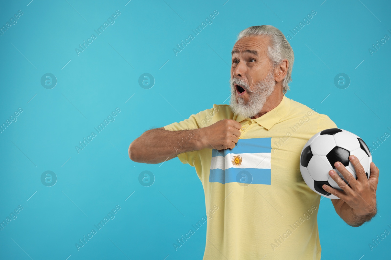 Excited fan with flag of Argentina on his polo shirt holding soccer ball against light blue background. Space for text Image of Excited fan with flag of Argentina on his polo shirt holding soccer ball against light blue background. Space for text