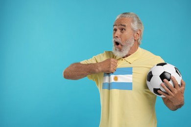 Image of Excited fan with flag of Argentina on his polo shirt holding soccer ball against light blue background. Space for text