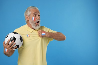 Image of Excited fan with flags of France painted on his body and polo shirt holding soccer ball against light blue background. Space for text