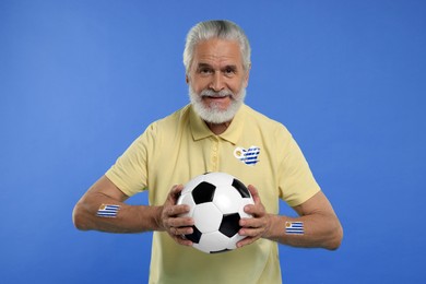 Image of Fan with flags of Uruguay on his body and polo shirt holding soccer ball against blue background