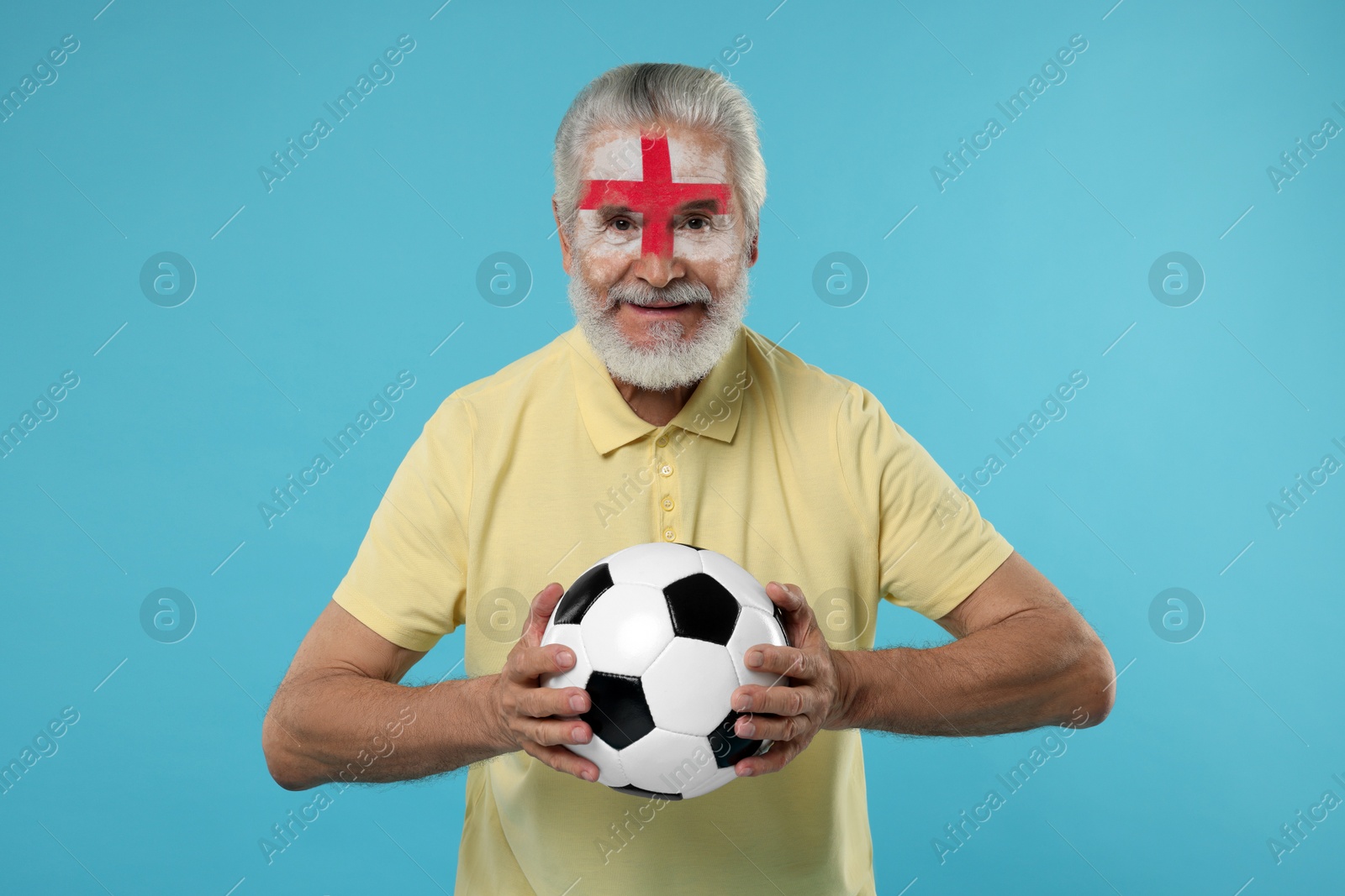 Fan with flag of England painted on his face holding soccer ball against light blue background Image of Fan with flag of England painted on his face holding soccer ball against light blue background