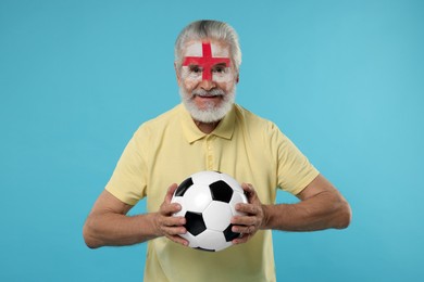 Image of Fan with flag of England painted on his face holding soccer ball against light blue background