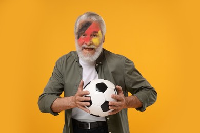 Image of Fan with flag of Germany painted on his face holding soccer ball against orange background