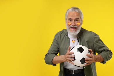 Image of Fan with colors matching Spain flag on his face and t-shirt holding soccer ball against yellow background. Space for text