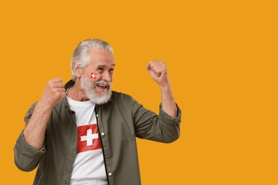Image of Excited fan with flags of Switzerland on his face and t-shirt against orange background. Space for text