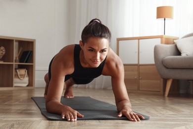 Image of Sporty woman doing plank exercise on fitness mat at home