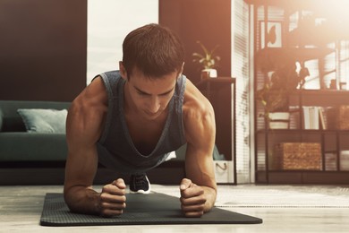 Image of Sporty man doing plank exercise on fitness mat at home