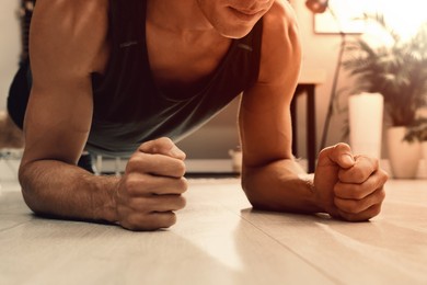 Image of Sporty man doing plank exercise on floor at home, closeup