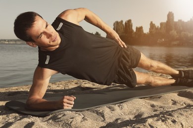 Image of Sporty man doing side plank exercise on beach outdoors