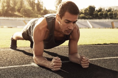 Image of Sporty man doing plank exercise at stadium