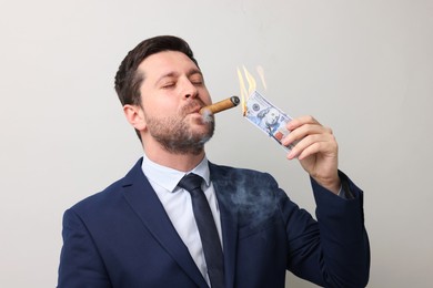 Image of Greedy businessman lighting cigar with dollar banknote on light grey background