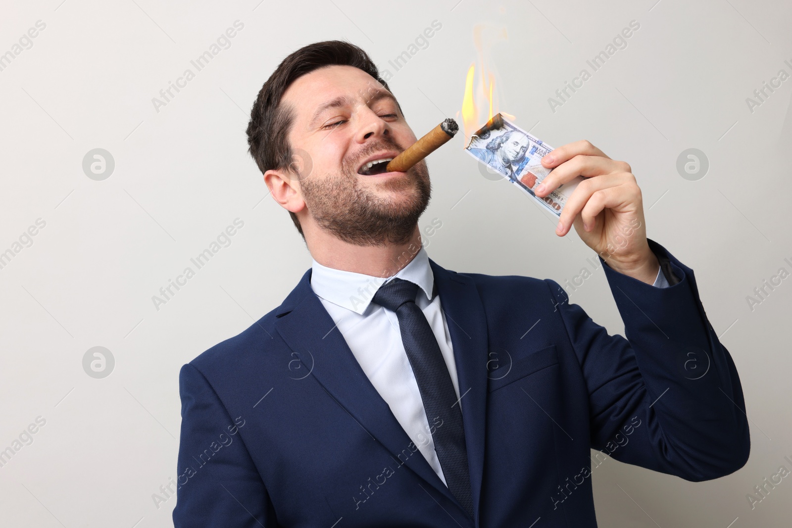 Greedy businessman lighting cigar with dollar banknote on light grey background Image of Greedy businessman lighting cigar with dollar banknote on light grey background