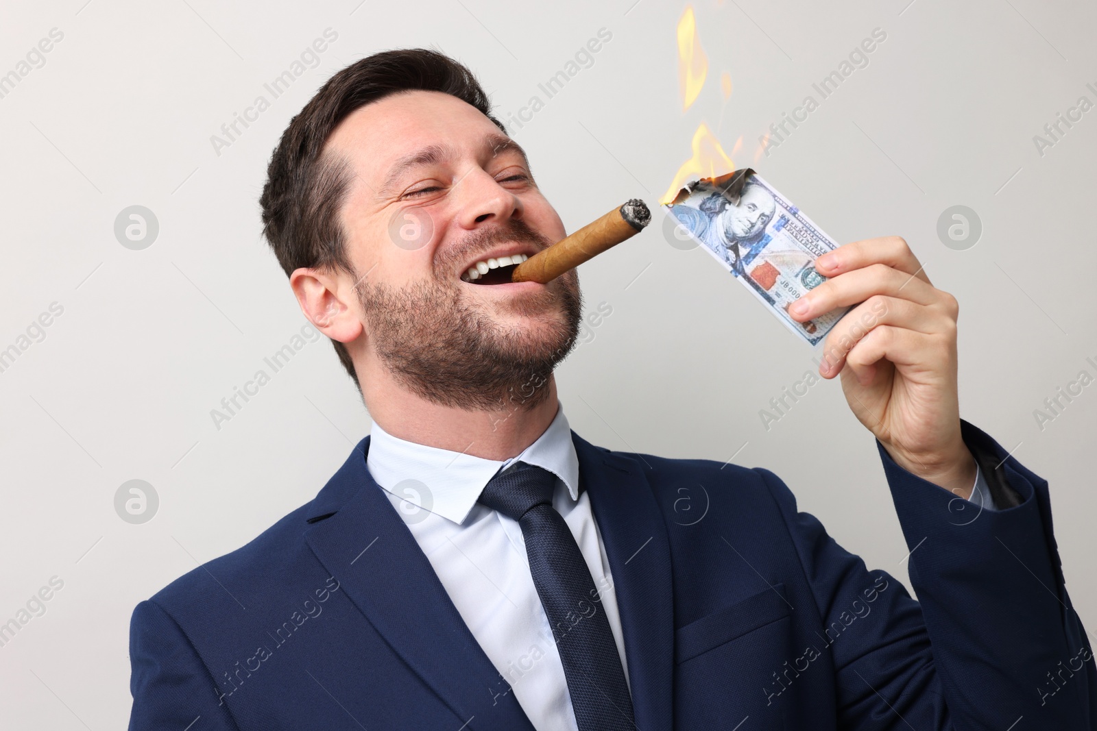 Greedy businessman lighting cigar with dollar banknote on light grey background Image of Greedy businessman lighting cigar with dollar banknote on light grey background