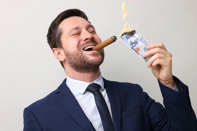 Image of Greedy businessman lighting cigar with dollar banknote on light grey background