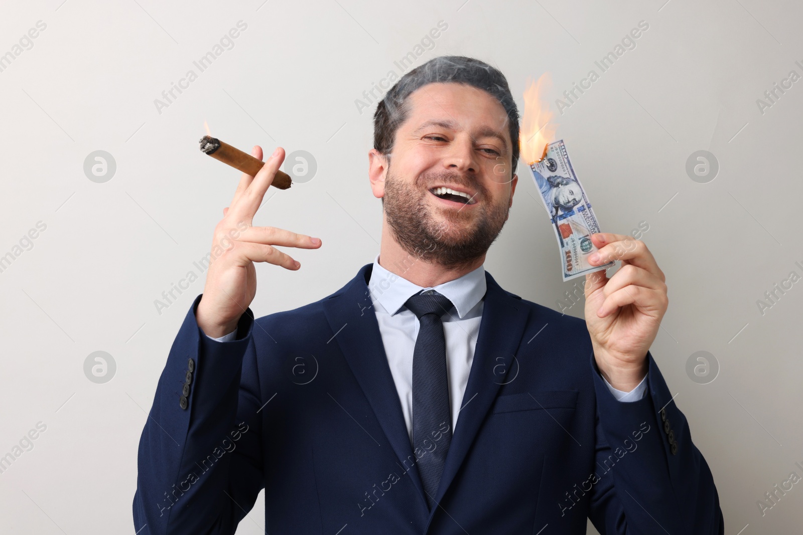 Greedy businessman with burning dollar banknote and cigar on light grey background Image of Greedy businessman with burning dollar banknote and cigar on light grey background