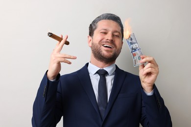 Image of Greedy businessman with burning dollar banknote and cigar on light grey background