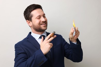 Image of Greedy businessman with burning dollar banknote and cigar on light grey background