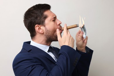 Image of Greedy businessman lighting cigar with dollar banknote on light grey background