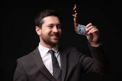 Image of Greedy businessman with burning dollar banknote on black background