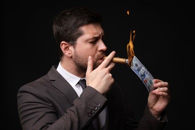 Image of Greedy businessman lighting cigar with dollar banknote on black background