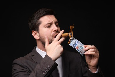 Image of Greedy businessman lighting cigar with dollar banknote on black background