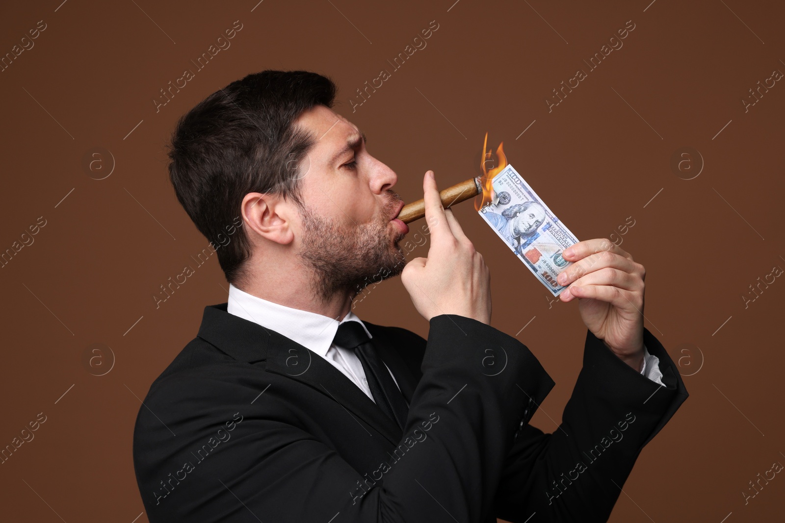 Greedy businessman lighting cigar with dollar banknote on brown background Image of Greedy businessman lighting cigar with dollar banknote on brown background