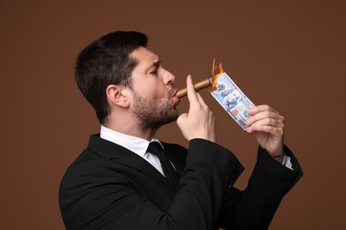 Image of Greedy businessman lighting cigar with dollar banknote on brown background