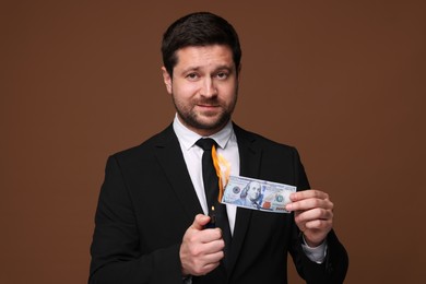 Image of Greedy businessman burning dollar banknote with lighter on brown background