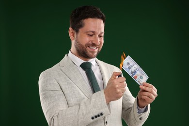 Image of Greedy businessman burning dollar banknote with lighter on dark green background