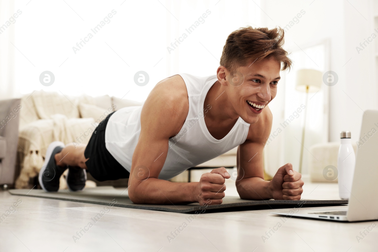 Sporty man doing plank exercise during online workout with coach via laptop at home Image of Sporty man doing plank exercise during online workout with coach via laptop at home