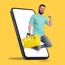 Image of Man with shopping basket jumping out of mobile phone against orange background. Online ordering
