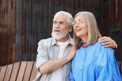Photo of Lovely senior couple on bench near building outdoors, space for text