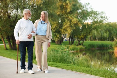 Photo of Lovely senior couple walking together near lake in park, space for text