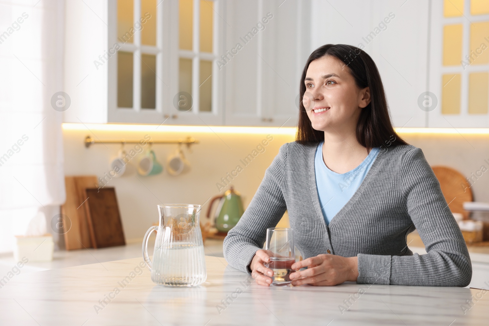 Woman with glass of water at white marble table in kitchen Photo of Woman with glass of water at white marble table in kitchen