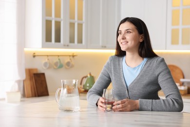 Photo of Woman with glass of water at white marble table in kitchen