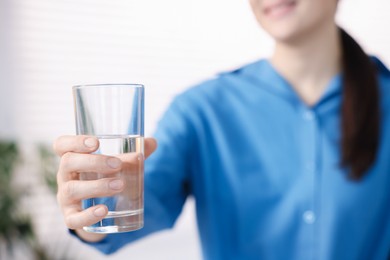 Photo of Woman drinking water from glass indoors, selective focus