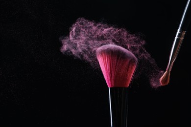 Photo of Makeup brushes with pink eye shadow on black background, closeup. Space for text