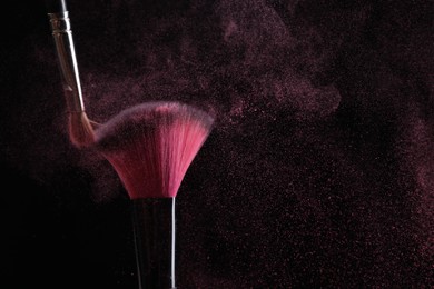 Photo of Makeup brushes with pink eye shadow on black background, closeup