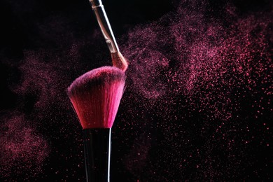 Photo of Makeup brushes with pink eye shadow on black background, closeup