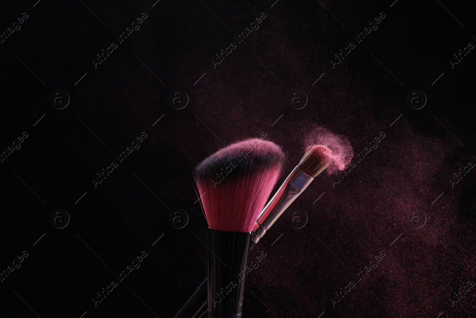 Makeup brushes with pink eye shadow on black background, closeup Photo of Makeup brushes with pink eye shadow on black background, closeup