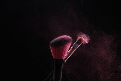 Photo of Makeup brushes with pink eye shadow on black background, closeup