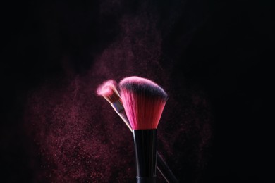Photo of Makeup brushes with pink eye shadow on black background, closeup