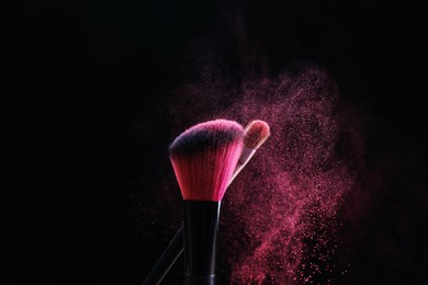 Photo of Makeup brushes with pink eye shadow on black background, closeup