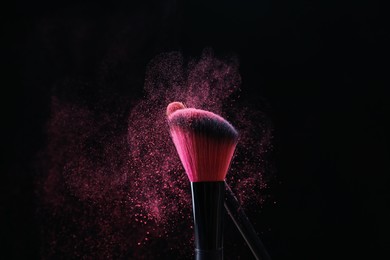 Photo of Makeup brushes with pink eye shadow on black background, closeup